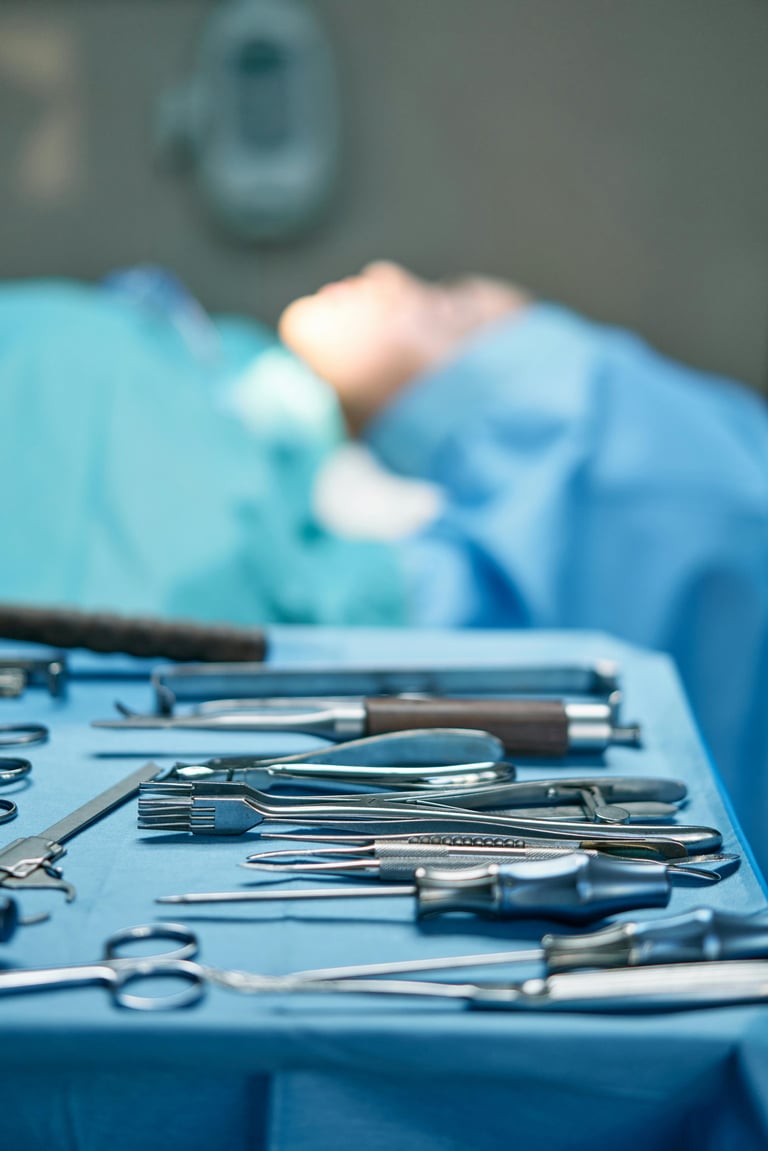 Sterile surgical instruments and tools laid out on blue medical drape with surgeon in background